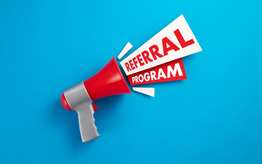 A red megaphone on a blue background emits paper cutouts with the words "Referral Program" in bold red and white letters.